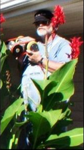 A man named Marvin is holding chimney cameras is standing next to a green plant with red flowers.